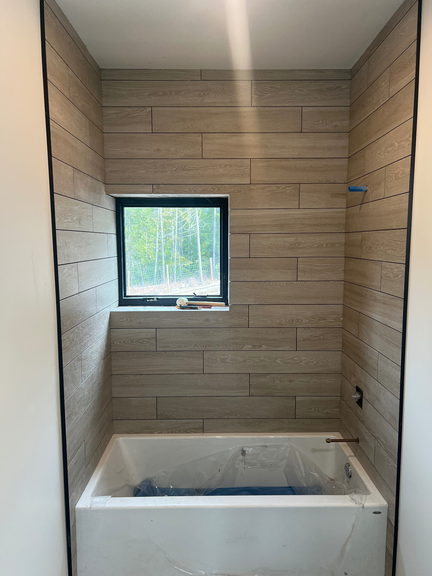 Tub surround in warm wood-look plank porcelain tile with black trim and window