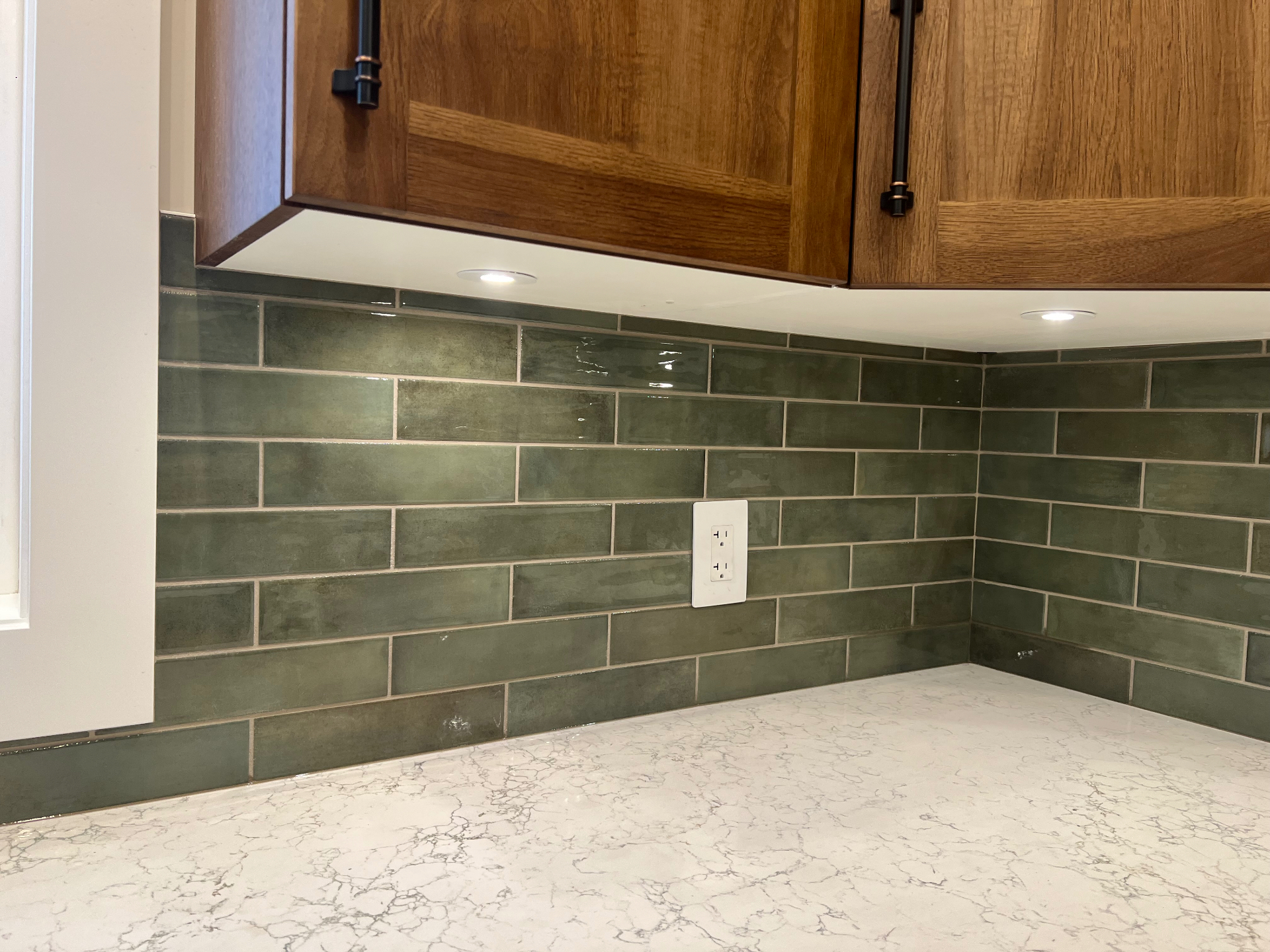 Glossy green elongated subway tile kitchen backsplash with walnut cabinetry and marble counter