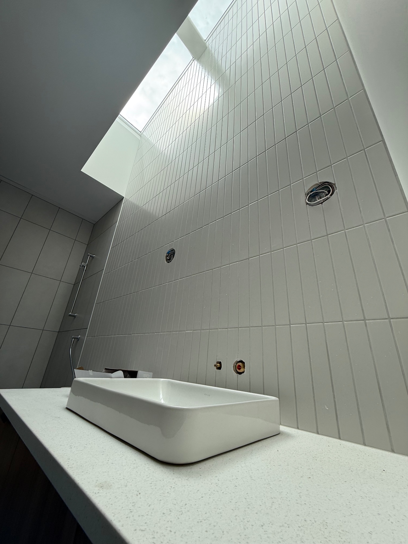 Vertical stack-bonded white tile bathroom wall under skylight