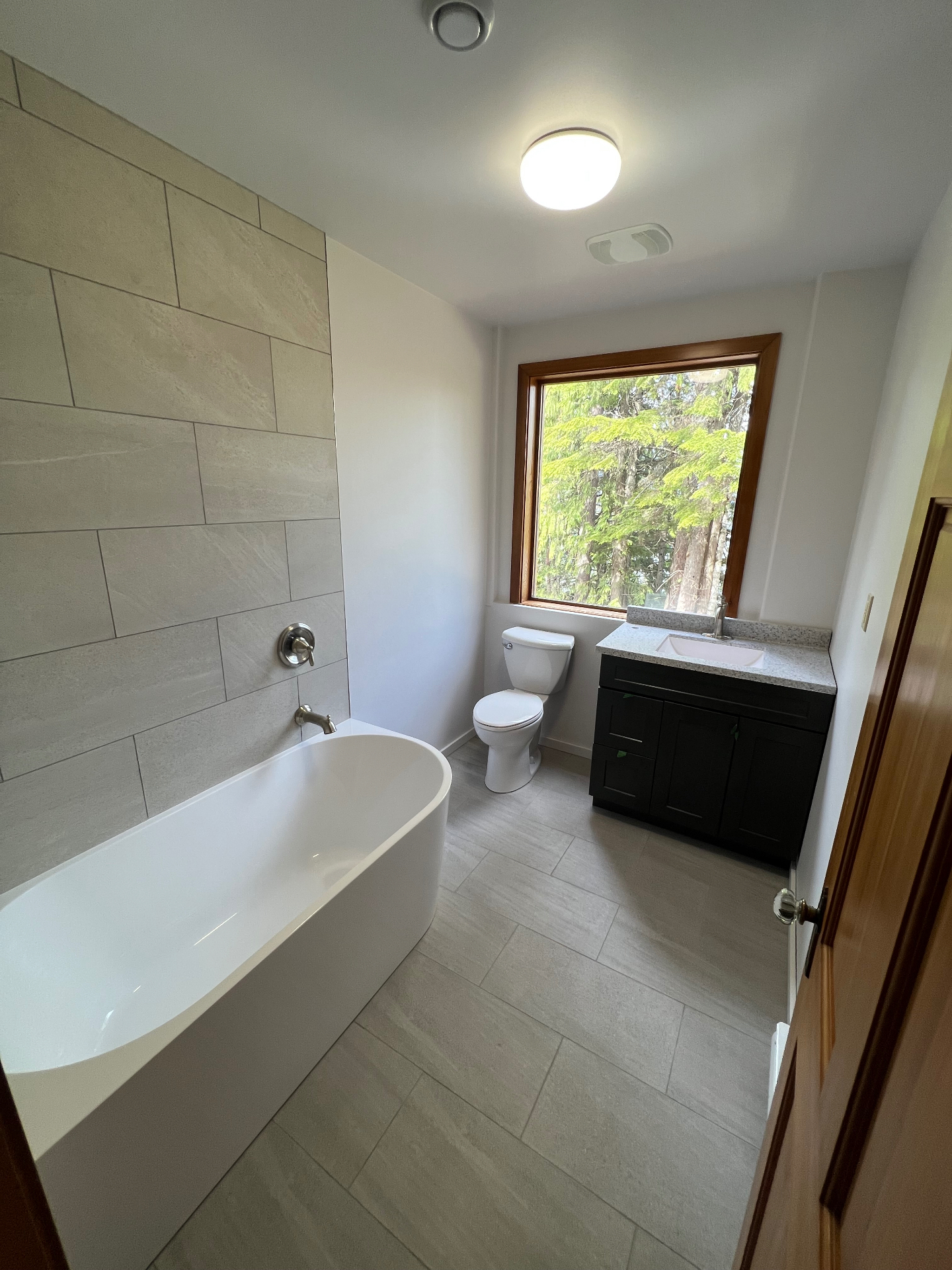 Bathroom with light stone-look large format wall tile, freestanding tub, and matching plank floor tile
