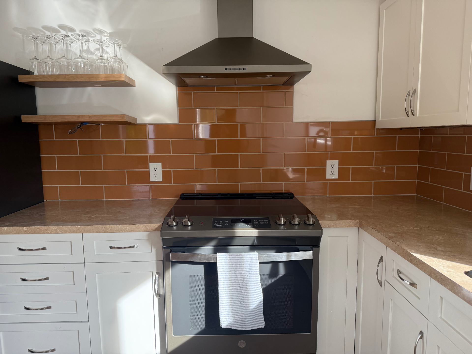 Warm terracotta orange subway tile backsplash behind range with floating wood shelves